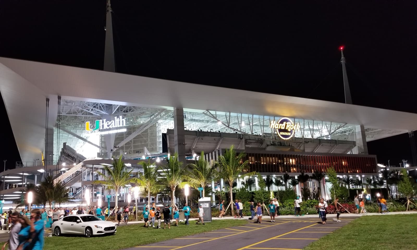 A stadium lit up at night with palm trees in front