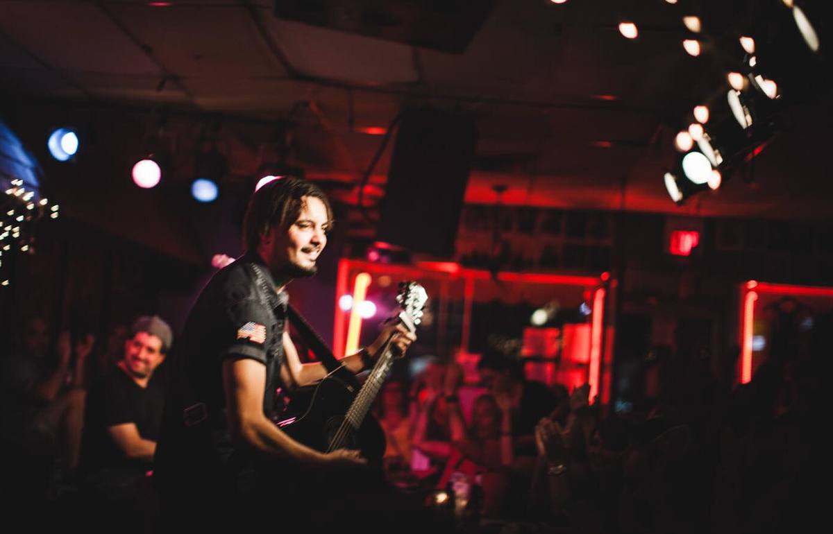 A singer with a guitar on a small low stage in a dark room strung with fairy lights