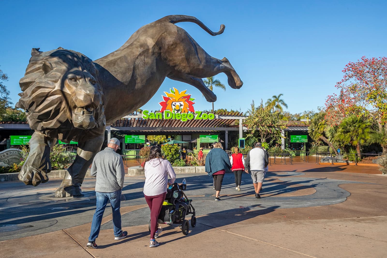 Visitors walk past a large bronze lion statue at the San Diego Zoo entrance