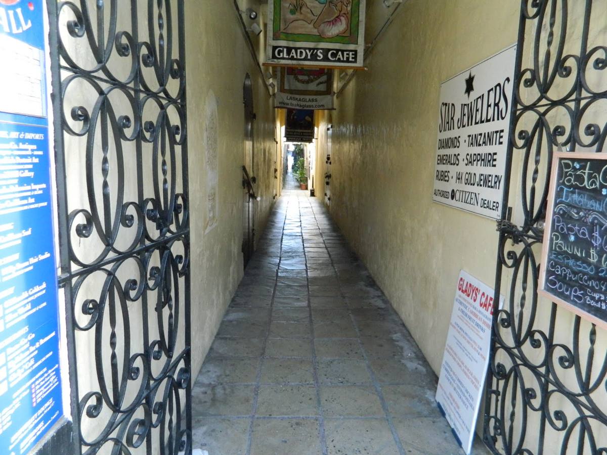 A narrow paved alley between old stone warehouse walls with shop signs