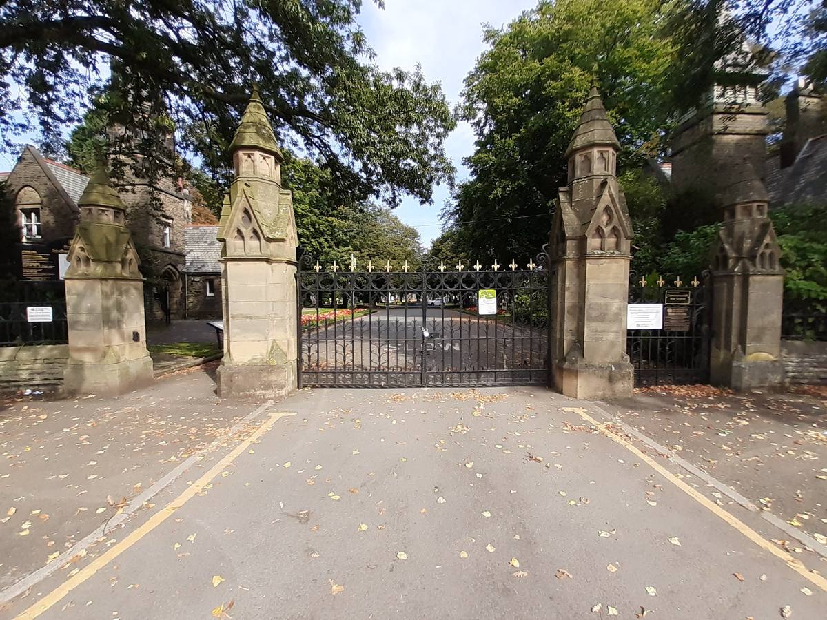 Stone gate piers and closed iron gates under trees, a road leading in