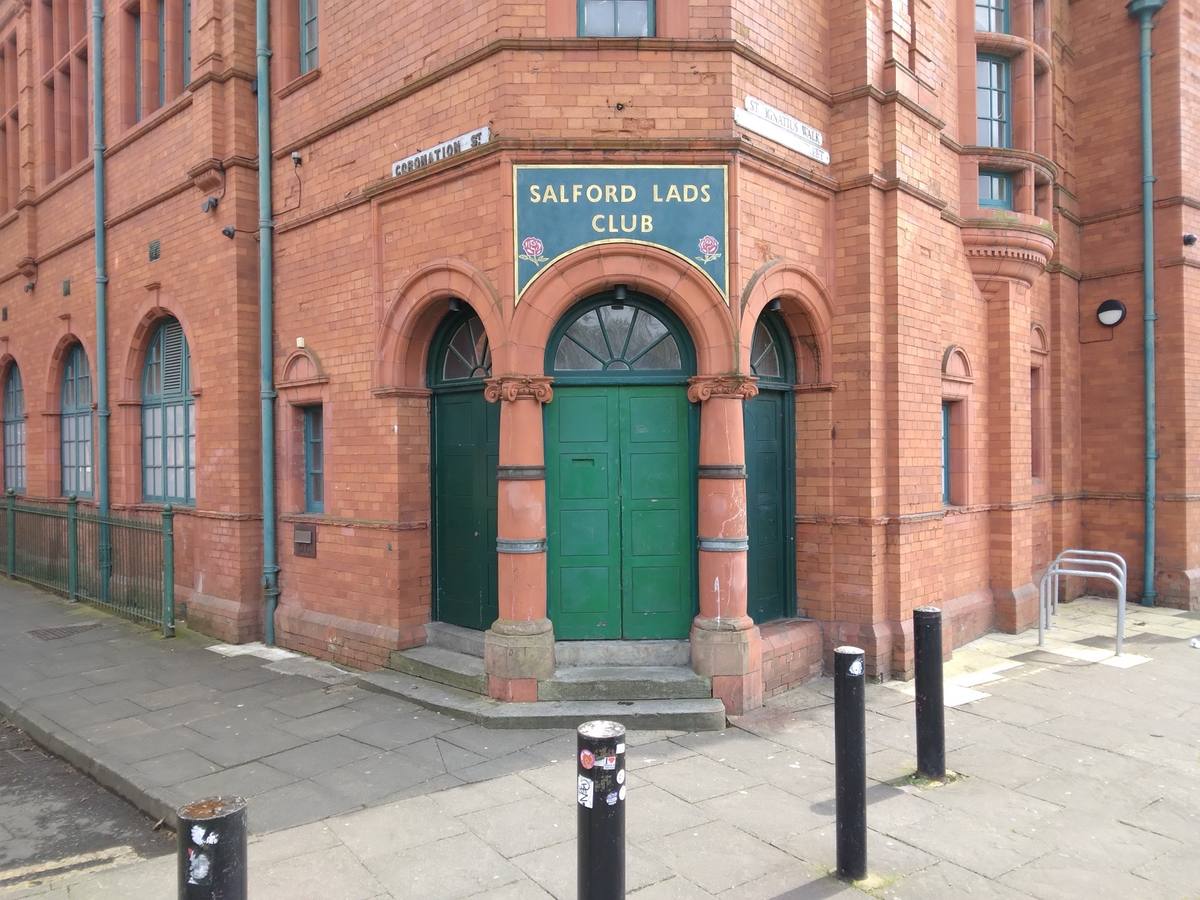 The red-brick corner entrance of Salford Lads Club, green double doors under its sign
