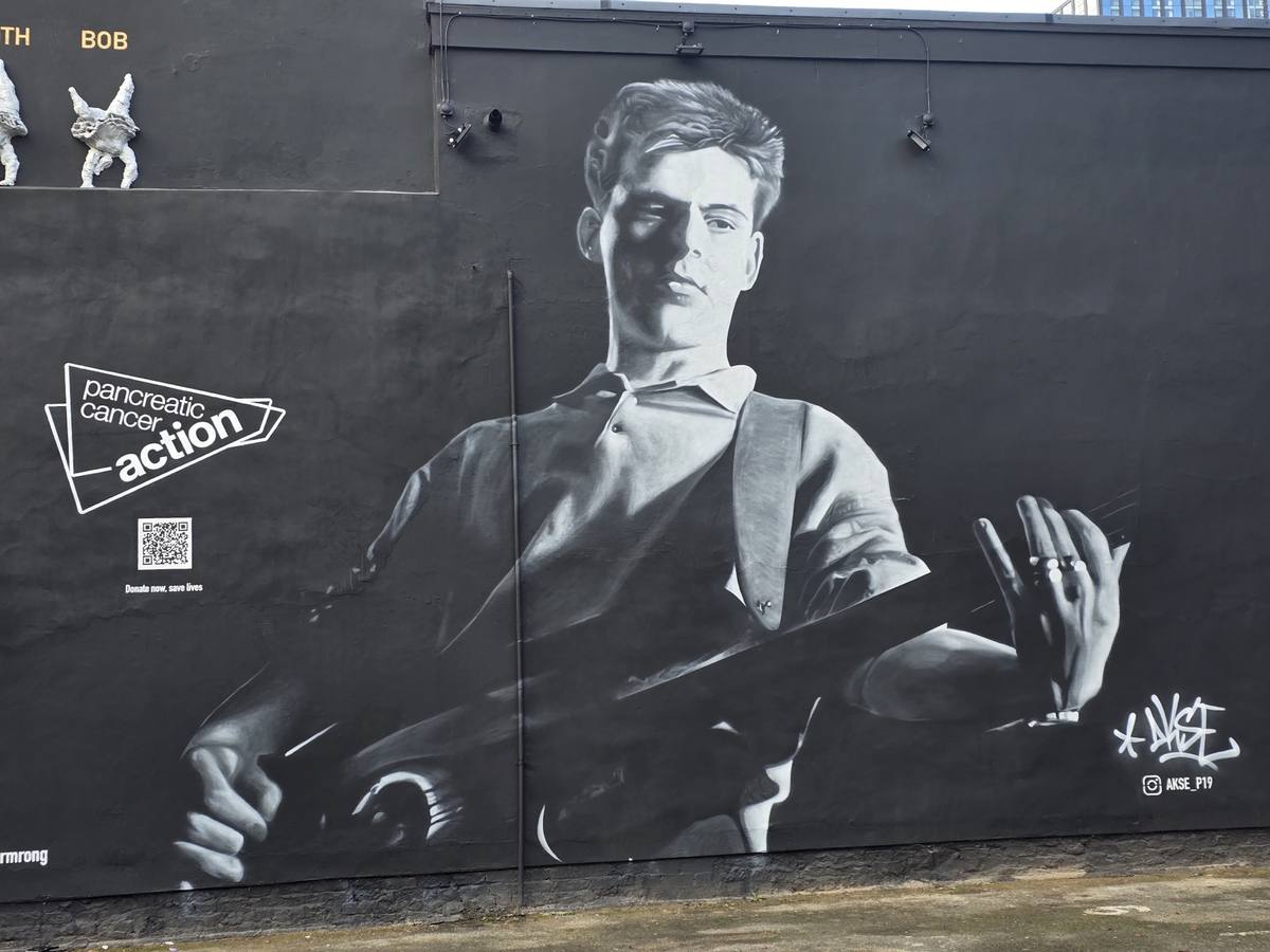 A huge black-and-white painted portrait of Andy Rourke with his bass on a black pub wall
