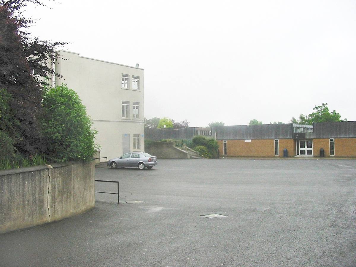 A wide tarmac school yard with low school buildings beyond it