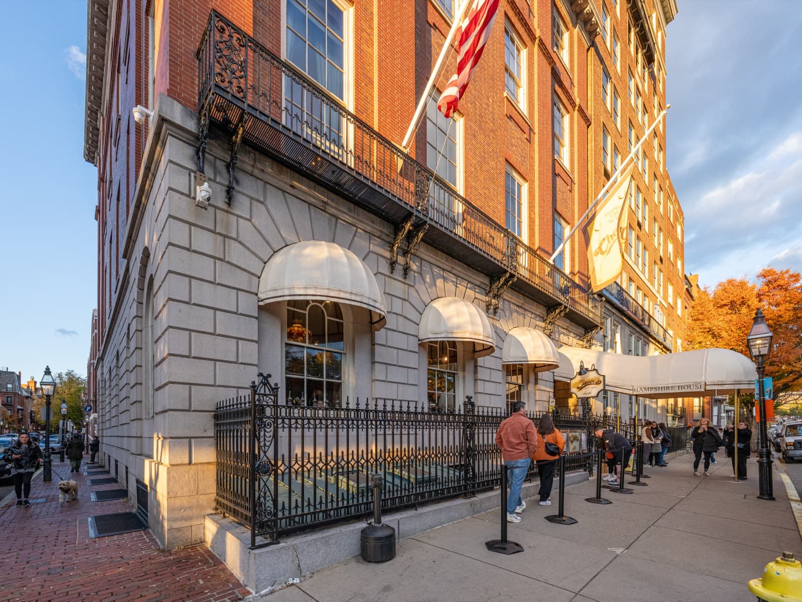 The stone lower storey of 84 Beacon Street in late sun, cream awnings over the pub windows and a queue along the railings