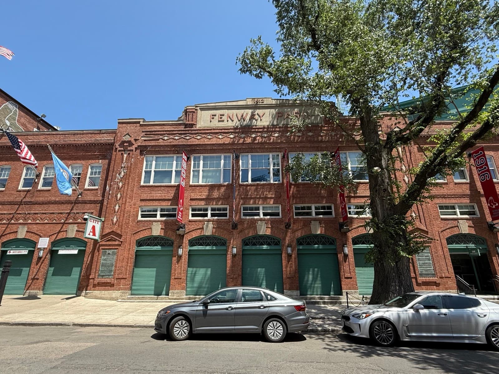 The red-brick front of Fenway Park with green doors and flags
