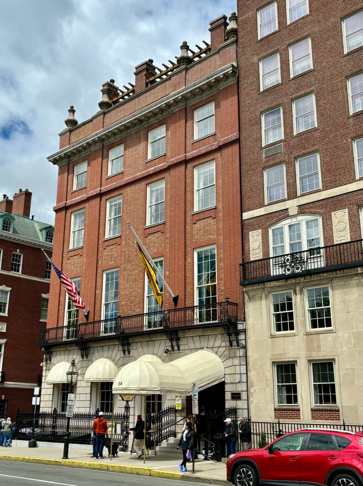 A five-storey red-brick and stone mansion with flags over a row of cream awnings