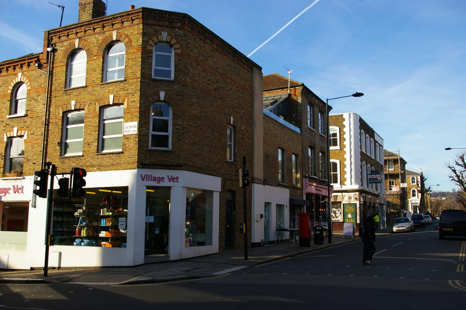 A residential street of terraced houses and small shops rising gently uphill