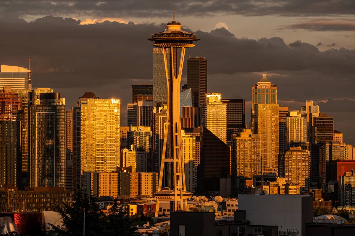 The Space Needle and gold-lit towers of downtown Seattle at sunset under dark cloud