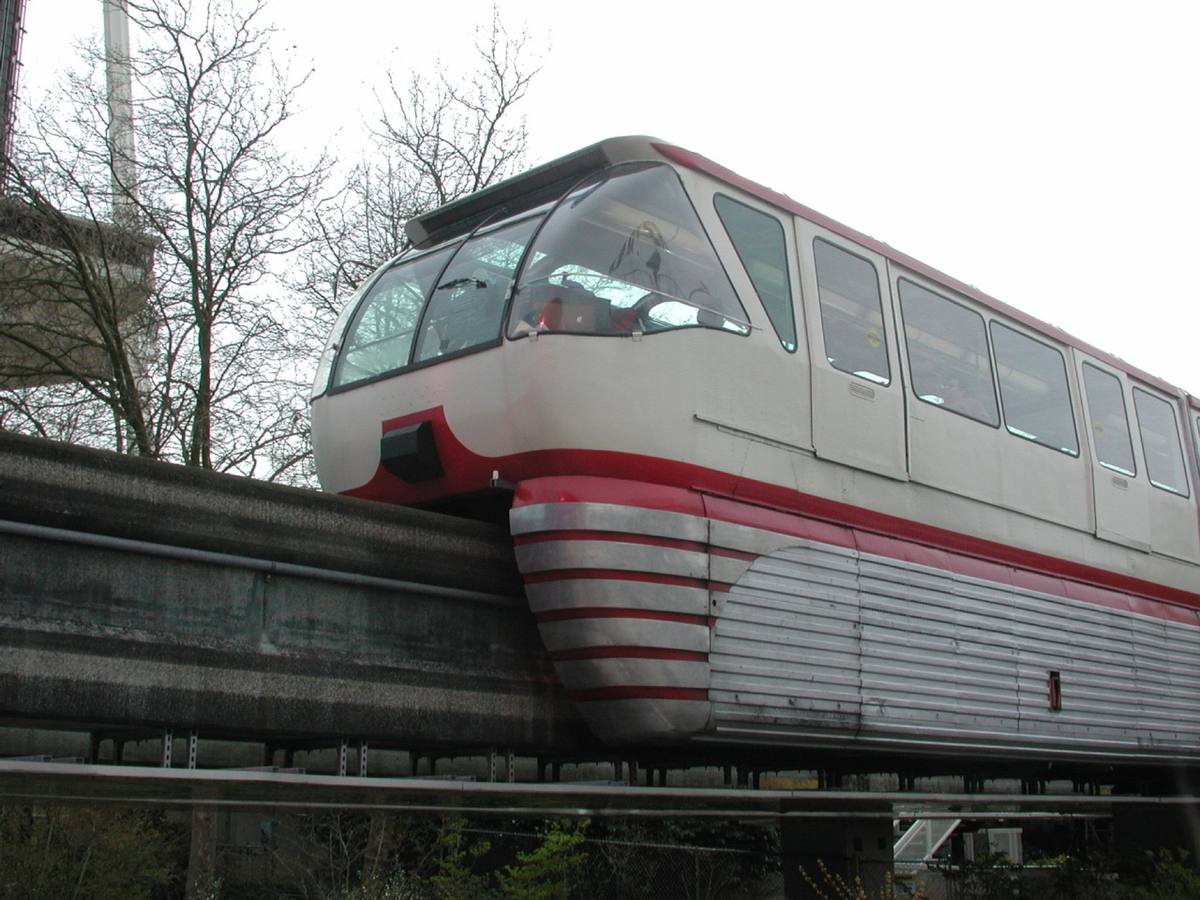 A silver and red monorail train on its concrete beam among trees