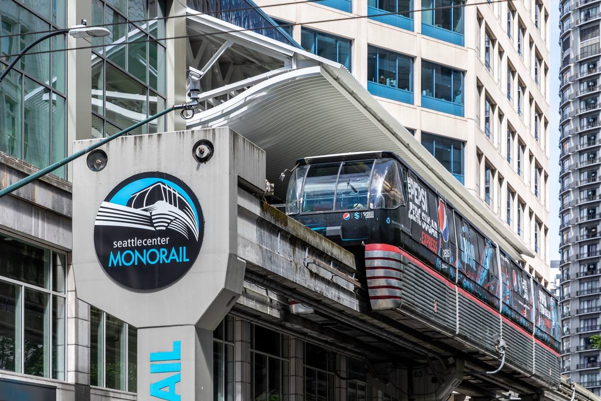 A monorail train under the canopy of the Westlake Center station, with the monorail sign