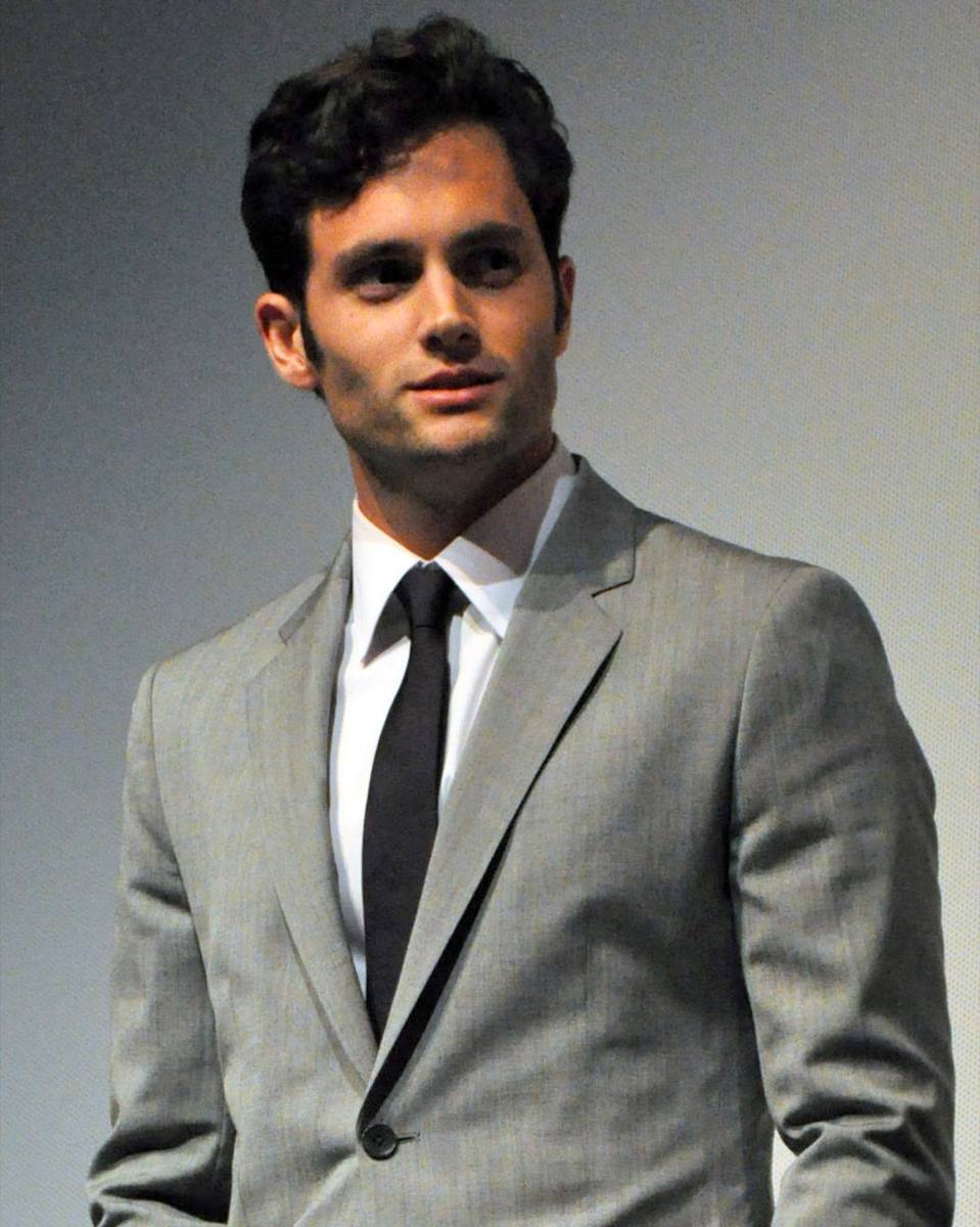 Penn Badgley with curly dark hair in an olive jacket, outdoors