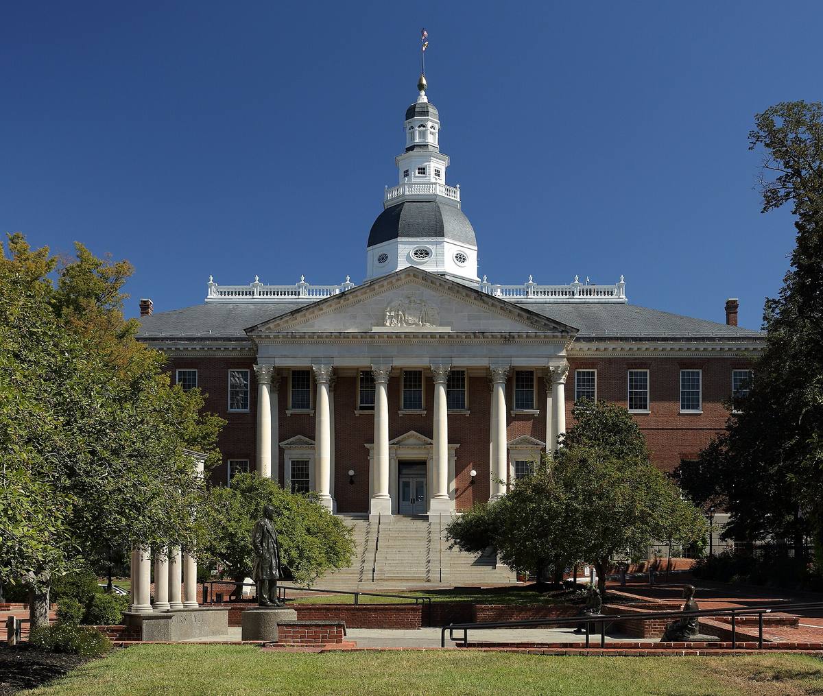 A red-brick capitol with a tall white wooden dome above trees