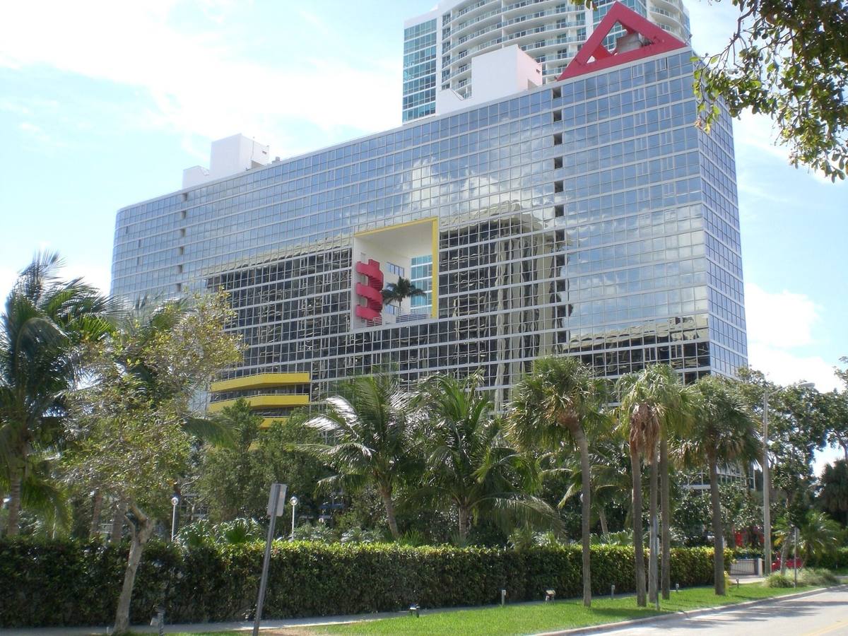 A blue glass tower with a square hole through the middle, a red stair and a palm inside