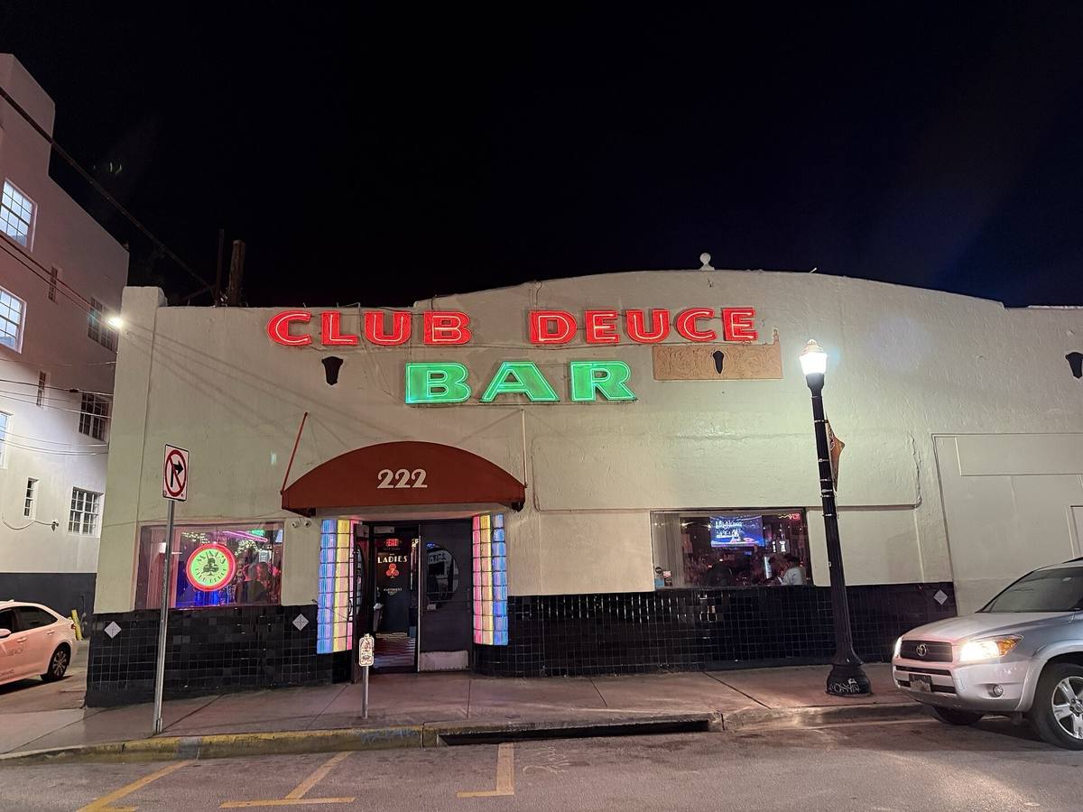 A low corner bar at night with red and green neon reading Club Deuce Bar
