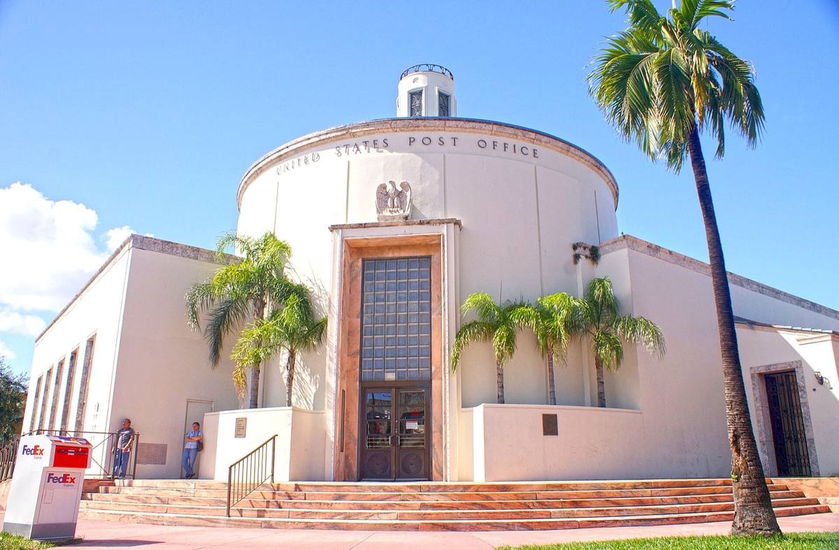 A round white Deco post office with a lantern on top and palms