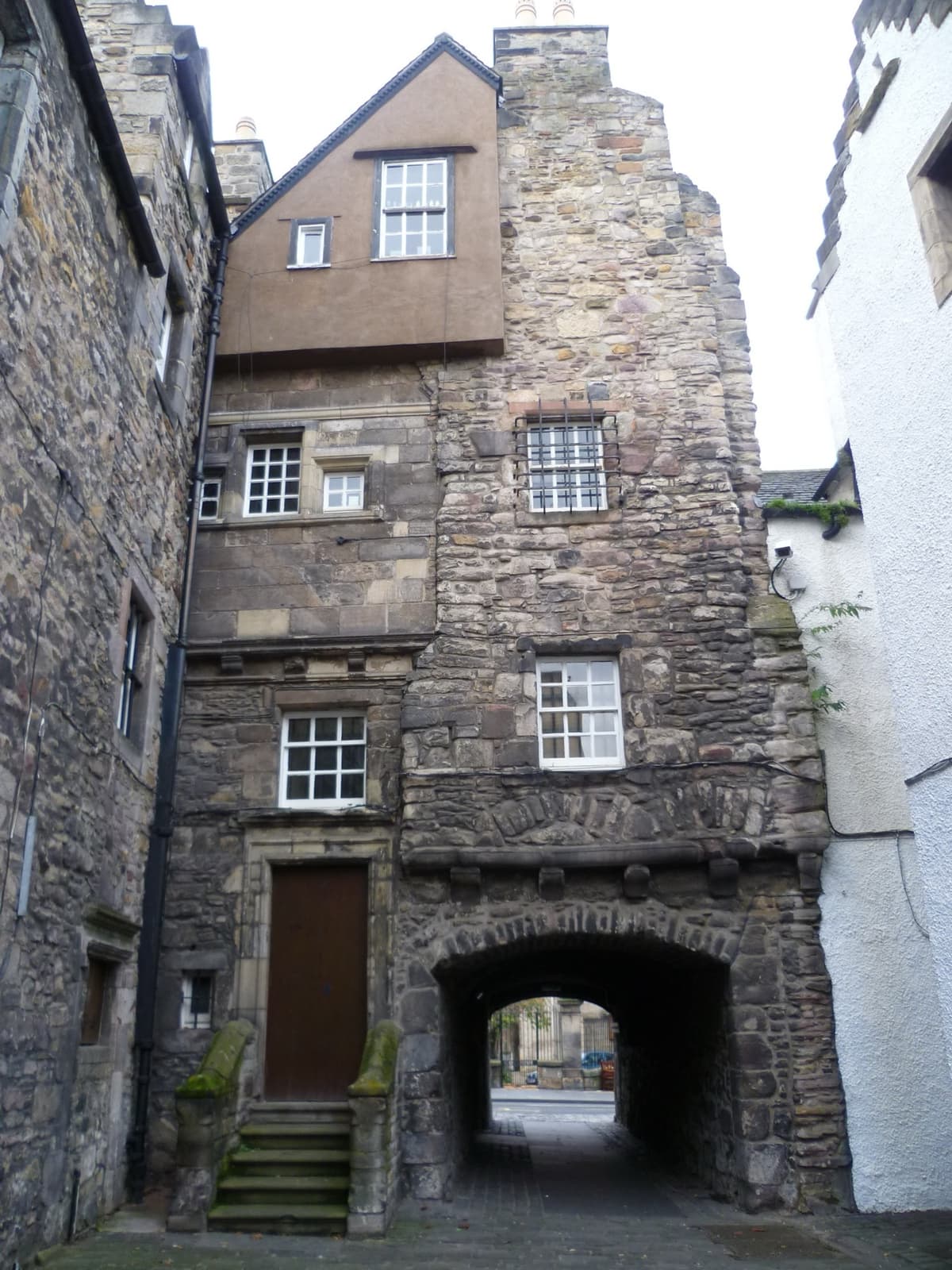 A tall stone house with a carved doorway over a pend in an Edinburgh close
