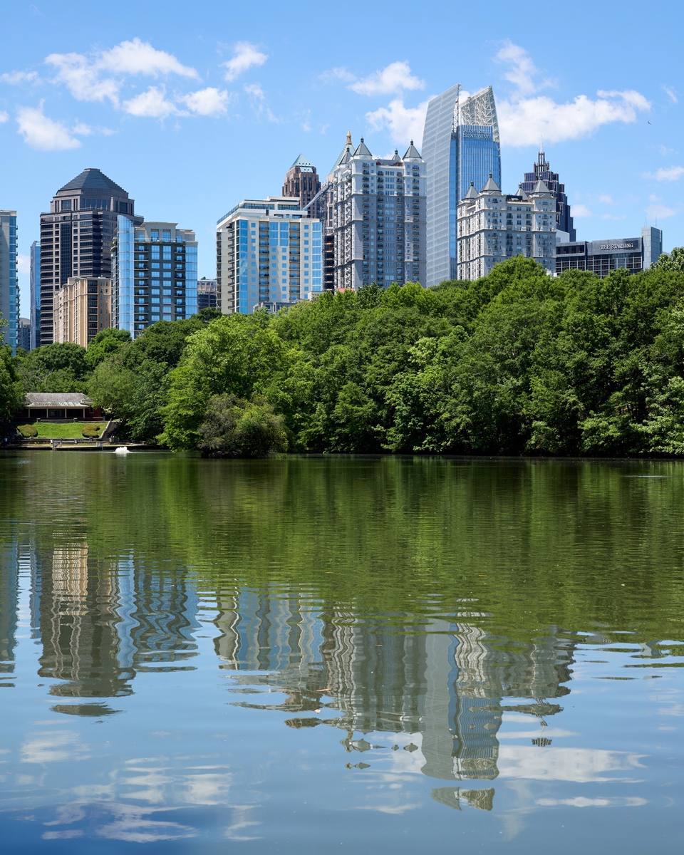 Midtown Atlanta towers reflected in a park lake behind a line of trees