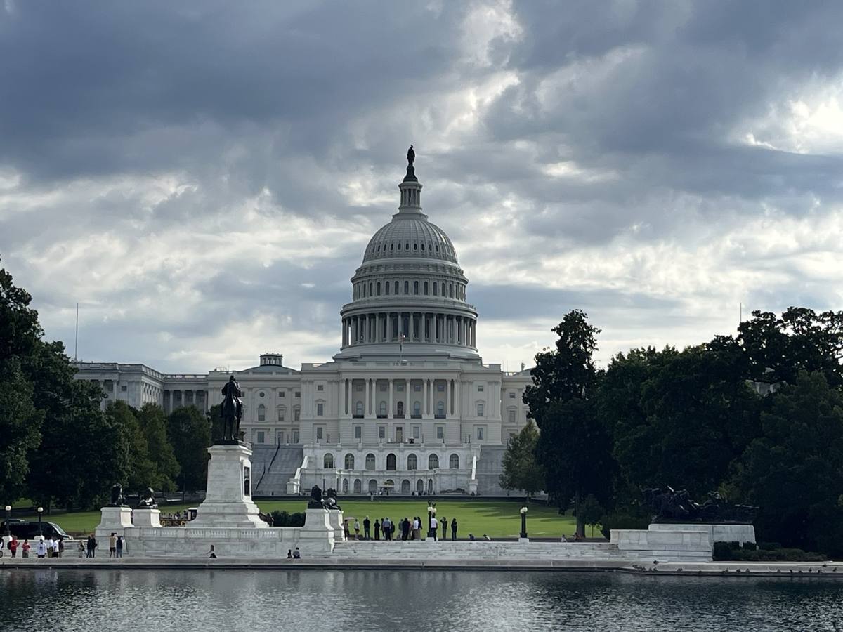 The domed Capitol beyond a long pool and a statue, under cloud