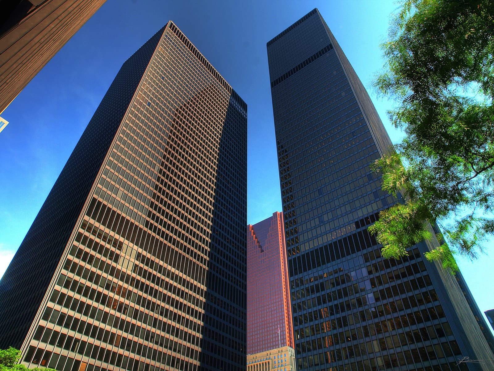 Black steel-and-glass towers seen from below against a blue sky