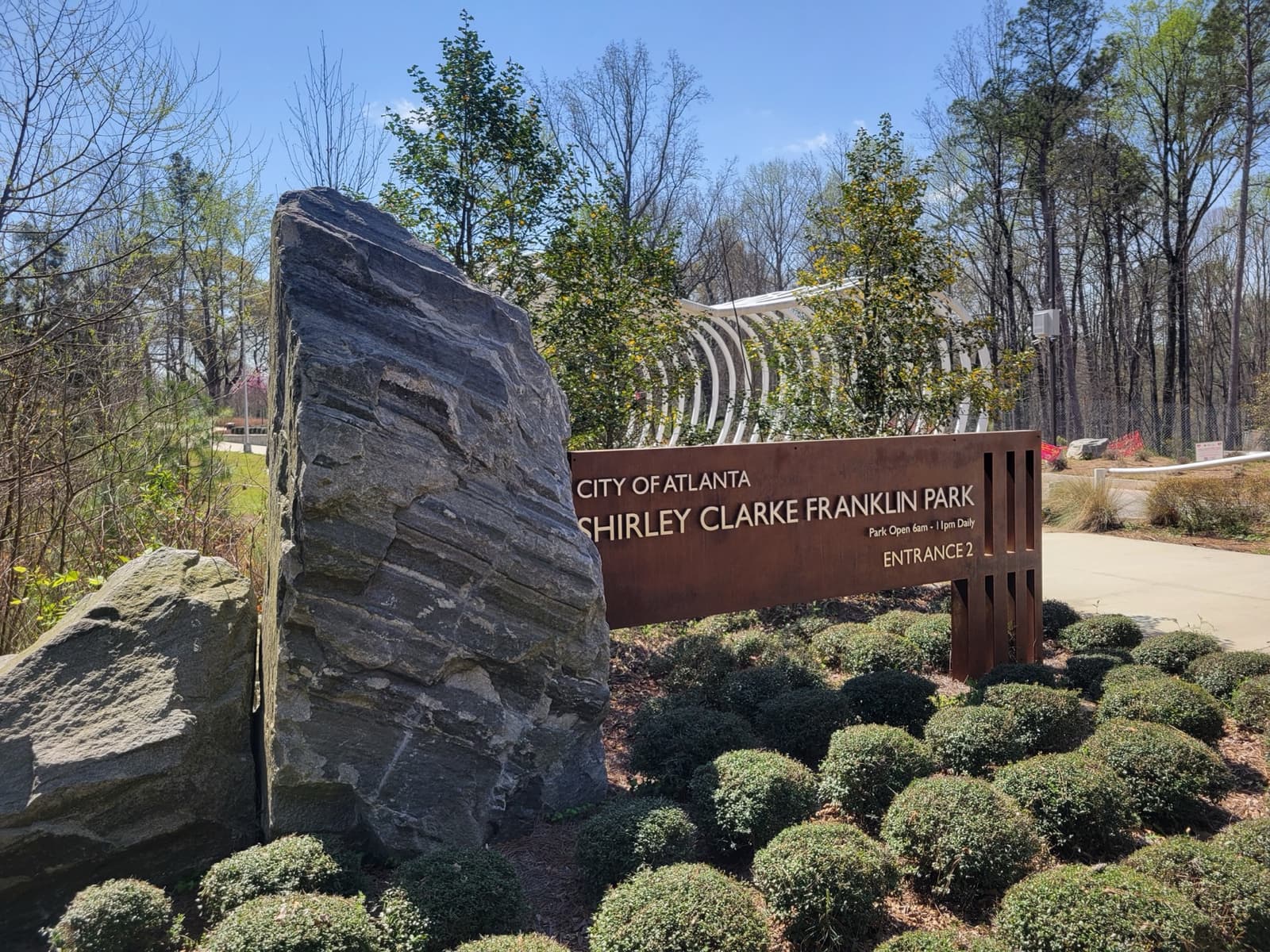 A tall slab of grey rock beside a park entrance sign and planted shrubs