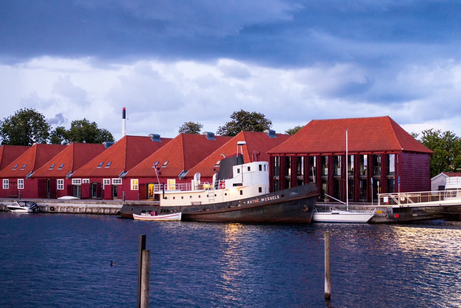 Red-roofed sheds along a harbour wall with an old boat moored in front