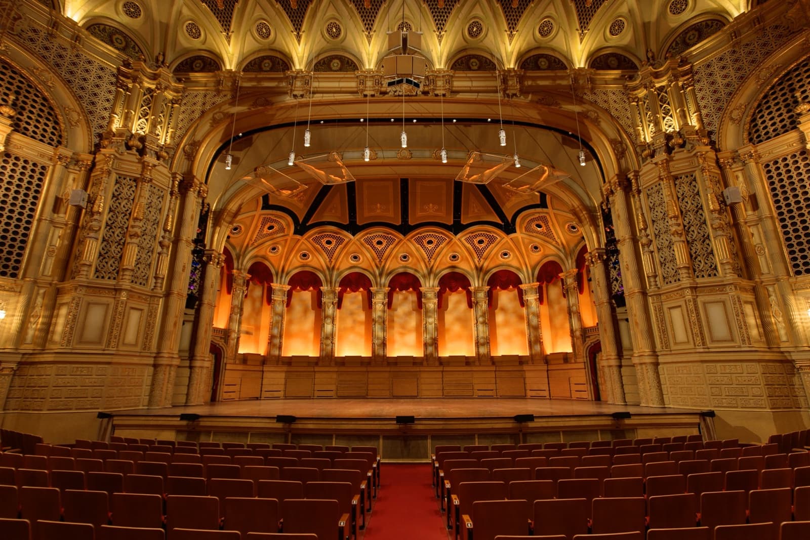 A gilded theatre auditorium with red seats facing an ornate lit stage