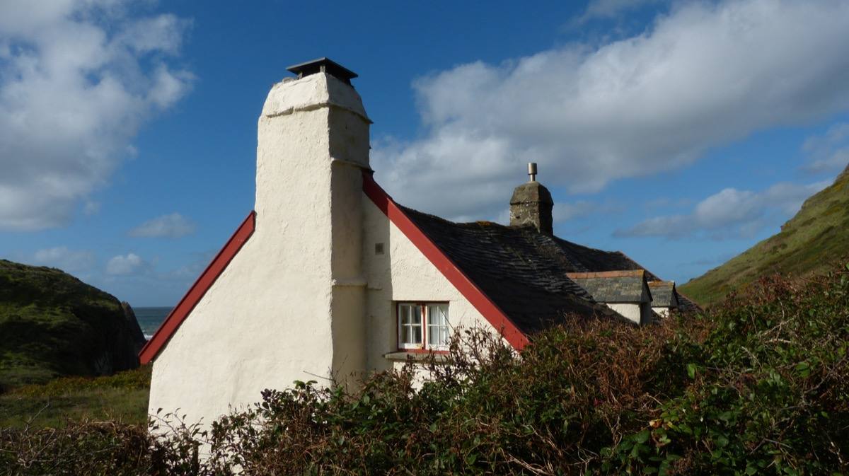 A lone stone cottage in a green valley above a pebble beach