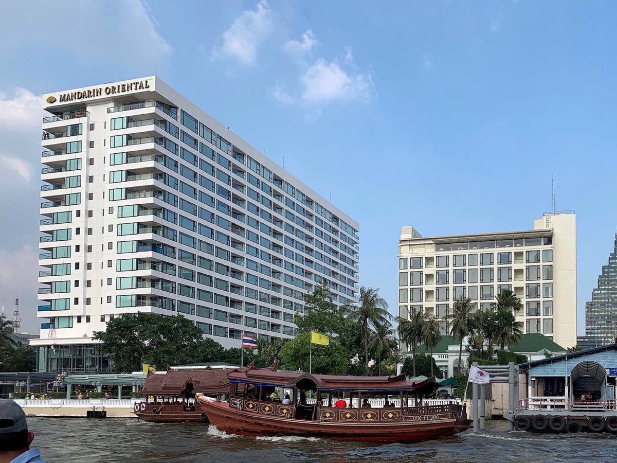 A white hotel tower on the riverbank with wooden long-tail boats moored in front