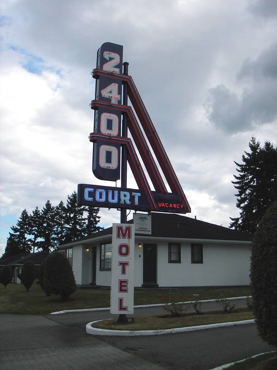 A tall neon sign reading 2400 Court Motel in front of a white bungalow cabin