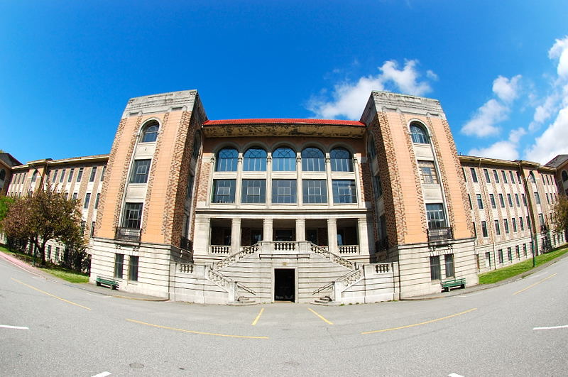 A symmetrical brick and stone hospital building with a grand central staircase, under a blue sky