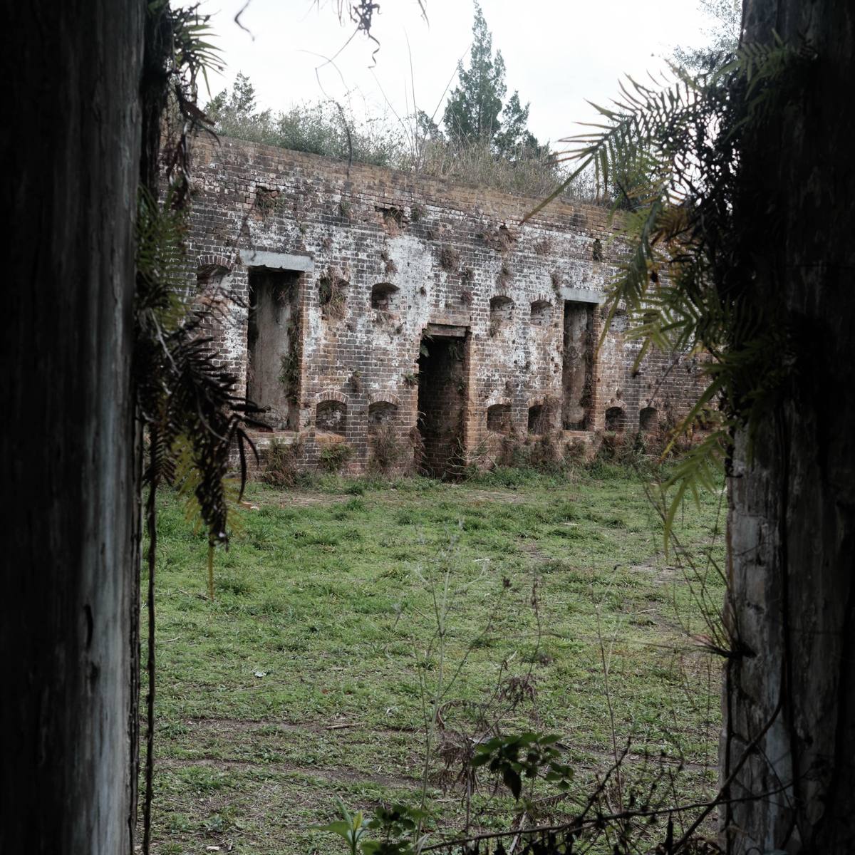 Brick casemates of a ruined fort seen through a dark archway, grass in the yard