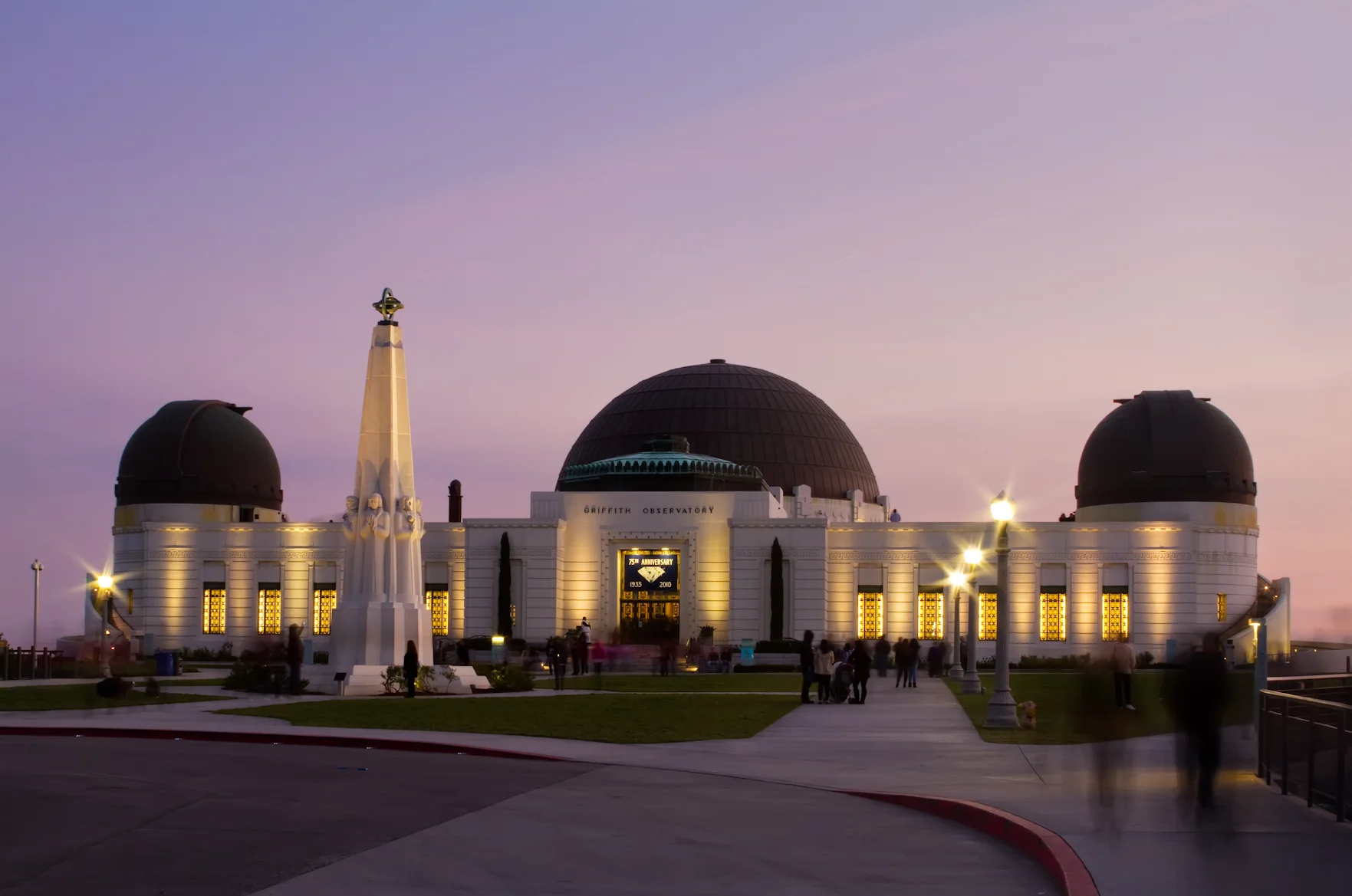 Griffith Observatory illuminated at dusk beneath a pink and violet sky.